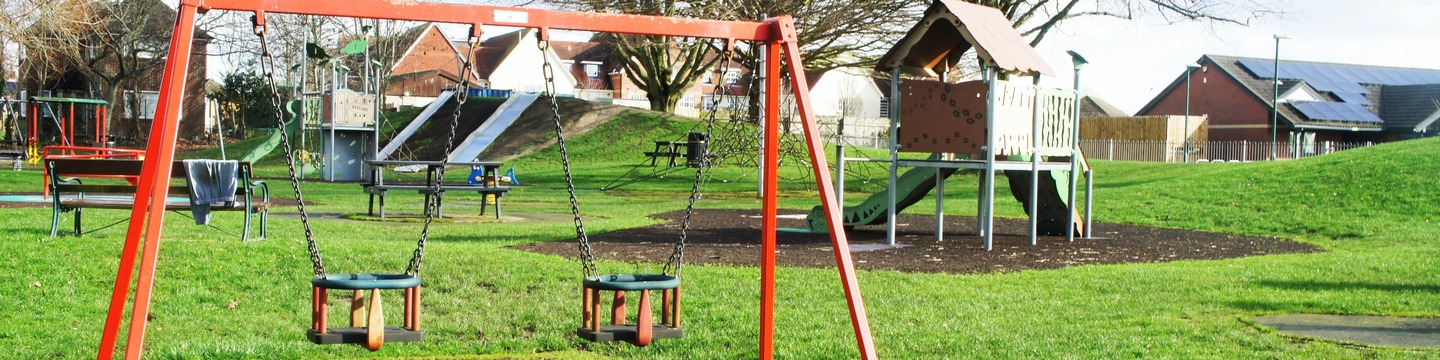 A picture of a play area with swings and other equipment in the background