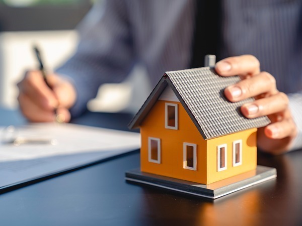 A hand holding a model house on a desk