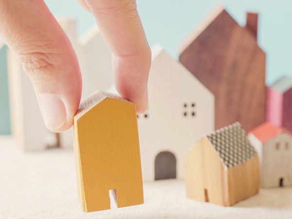 A hand is placing a smalle wooden model of a house, among other differing wooden models of buildings